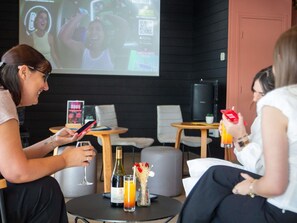 A group of people seated around a table with drinks, a wine bottle, and a projector screen in the background.