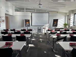 A conference room with white tables, black chairs, a large screen, and posters on the walls. - ibis Lyon Sud Oullins (Oullins)