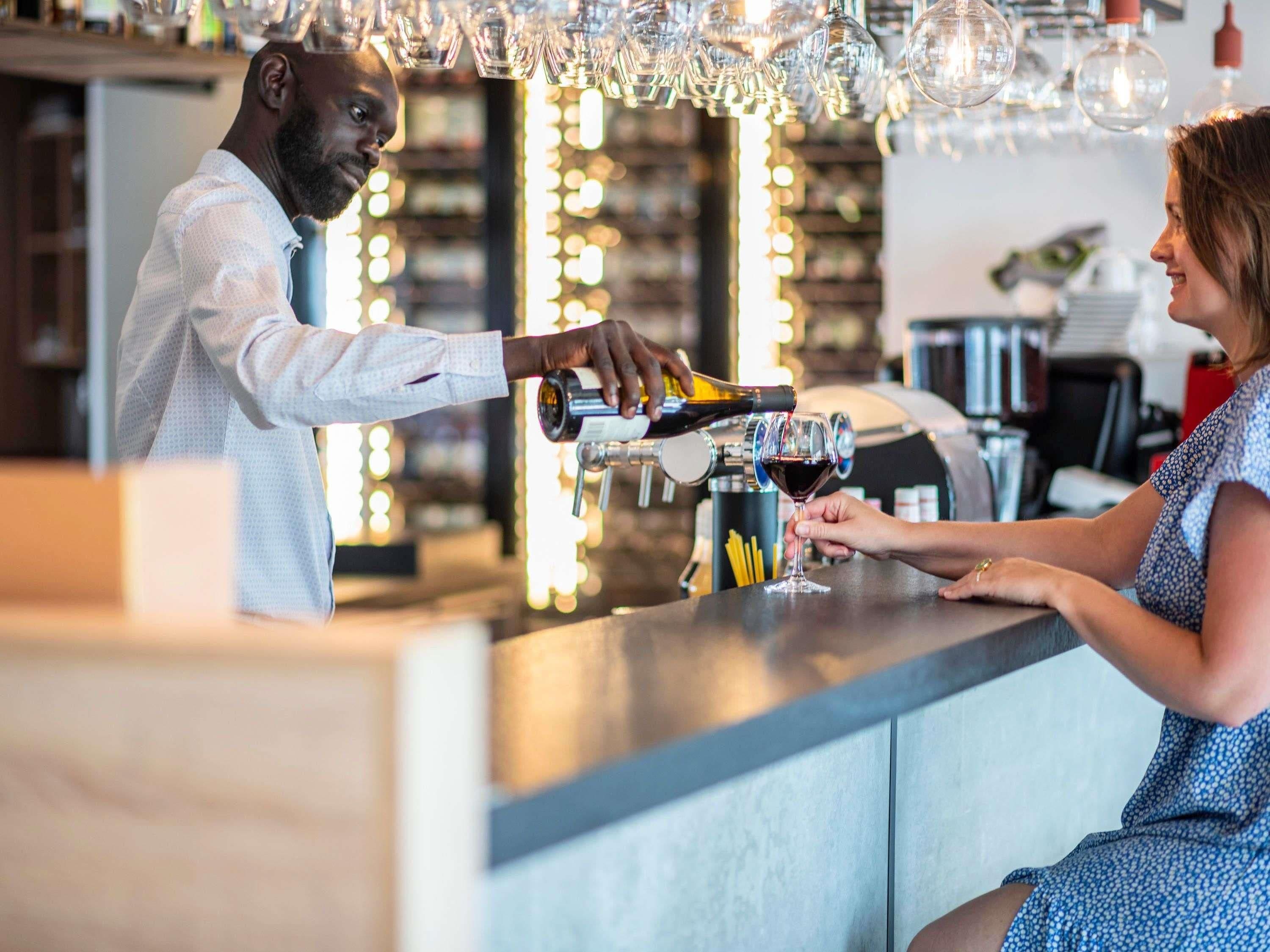 A bar setting with a bartender pouring a drink into a glass.