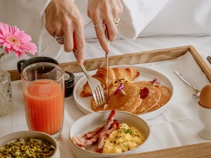 A breakfast tray with pancakes, croissants, scrambled eggs, and bacon.