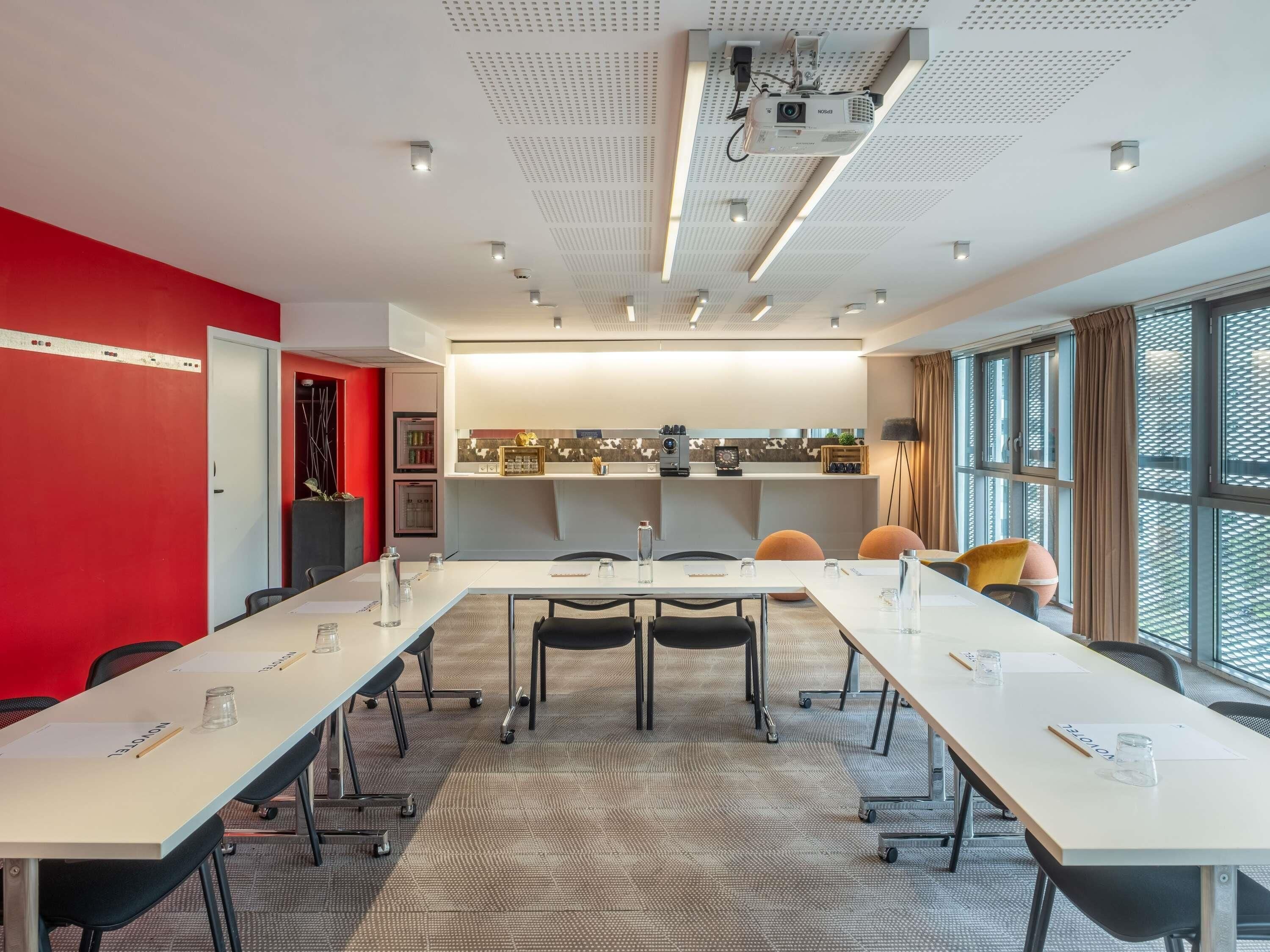 A conference room with a long table, chairs, a projector, and a kitchenette area.