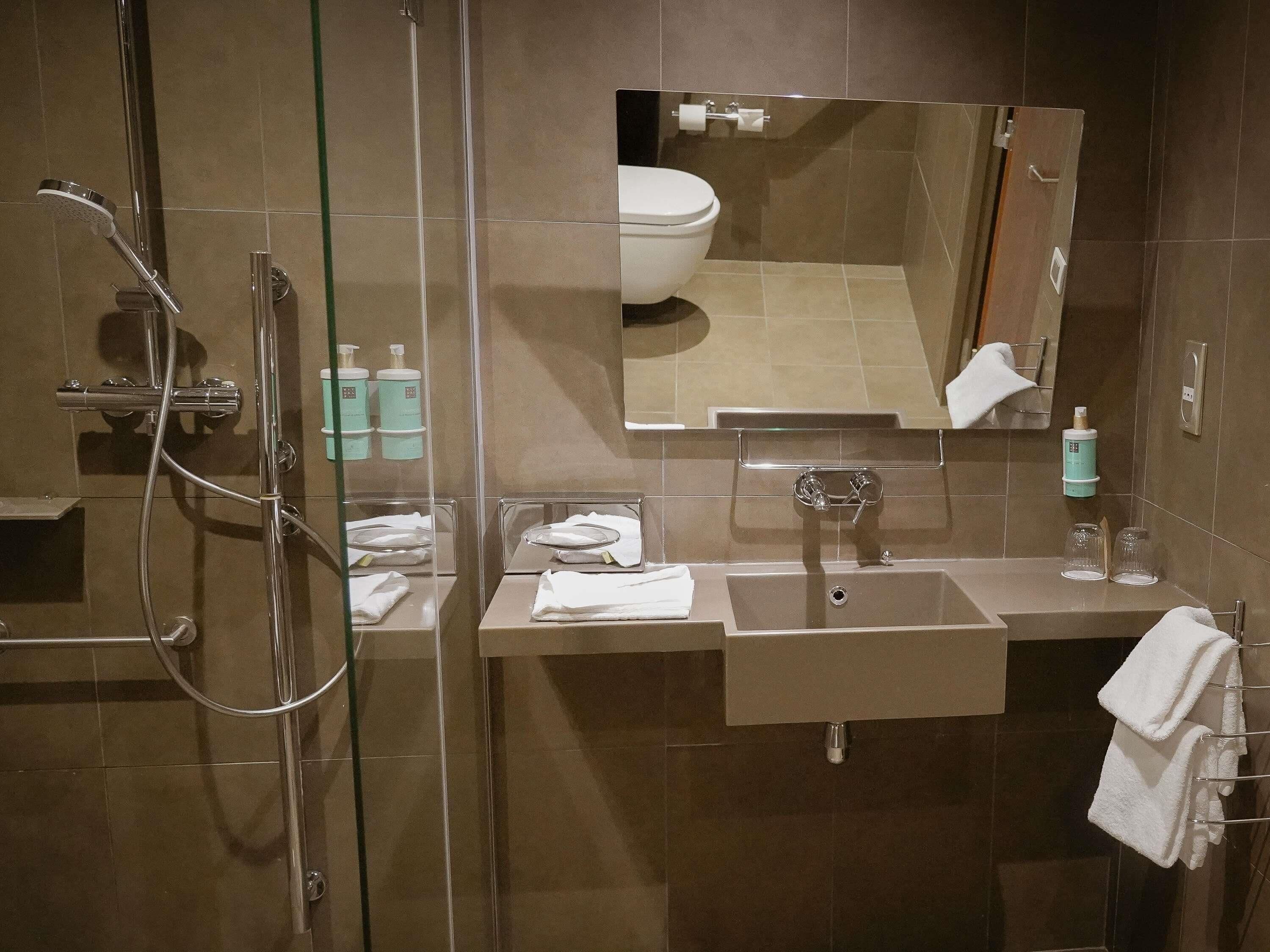 A modern bathroom with a glass shower enclosure, a sink with a mirror above it, and a towel rack.