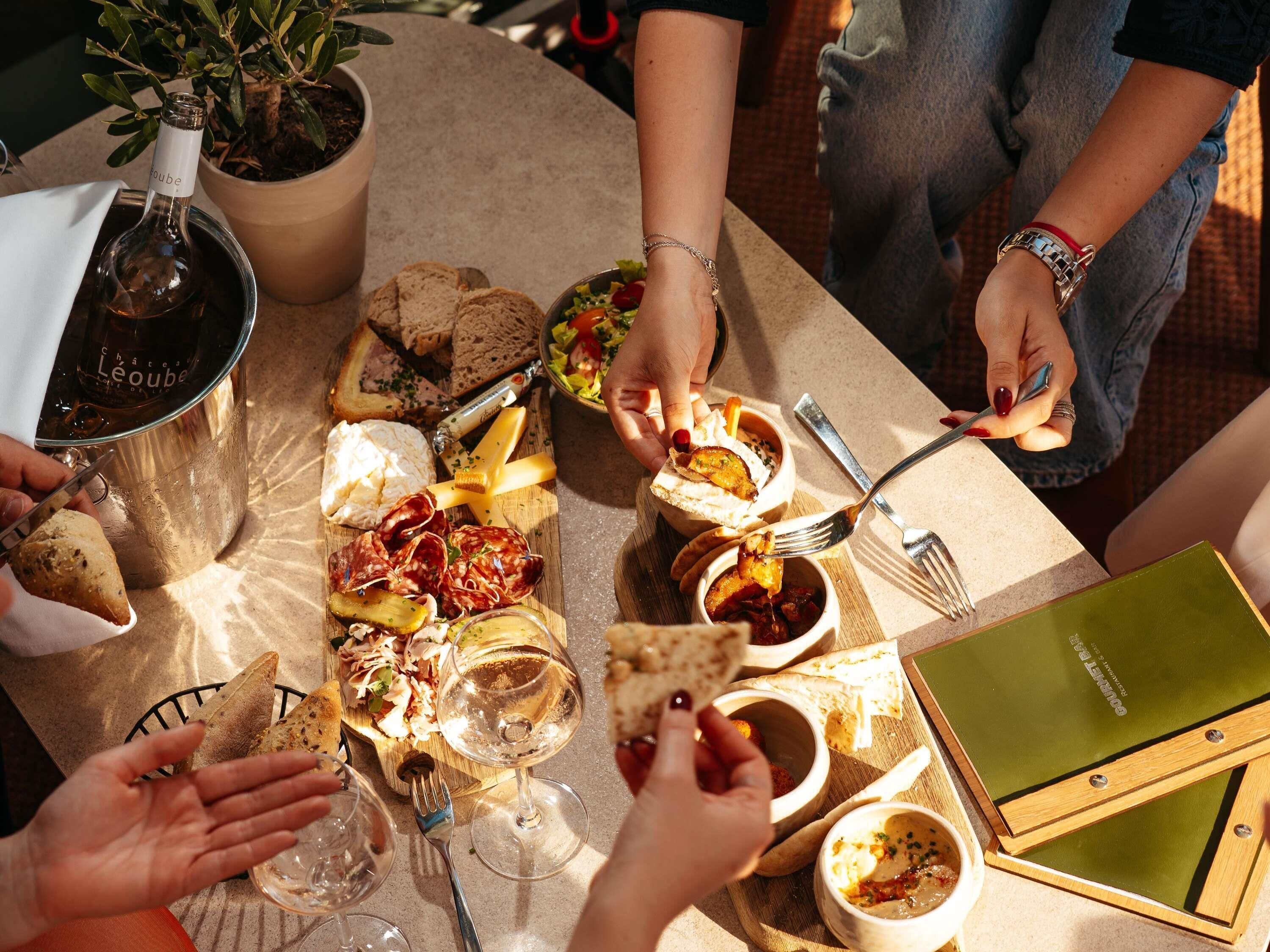 Un grupo de personas cenando en una mesa con diversos alimentos, como pan, queso y una botella de vino.