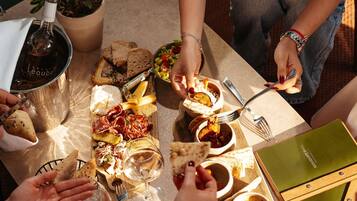 Un grupo de personas cenando en una mesa con diversos alimentos, como pan, queso y una botella de vino.