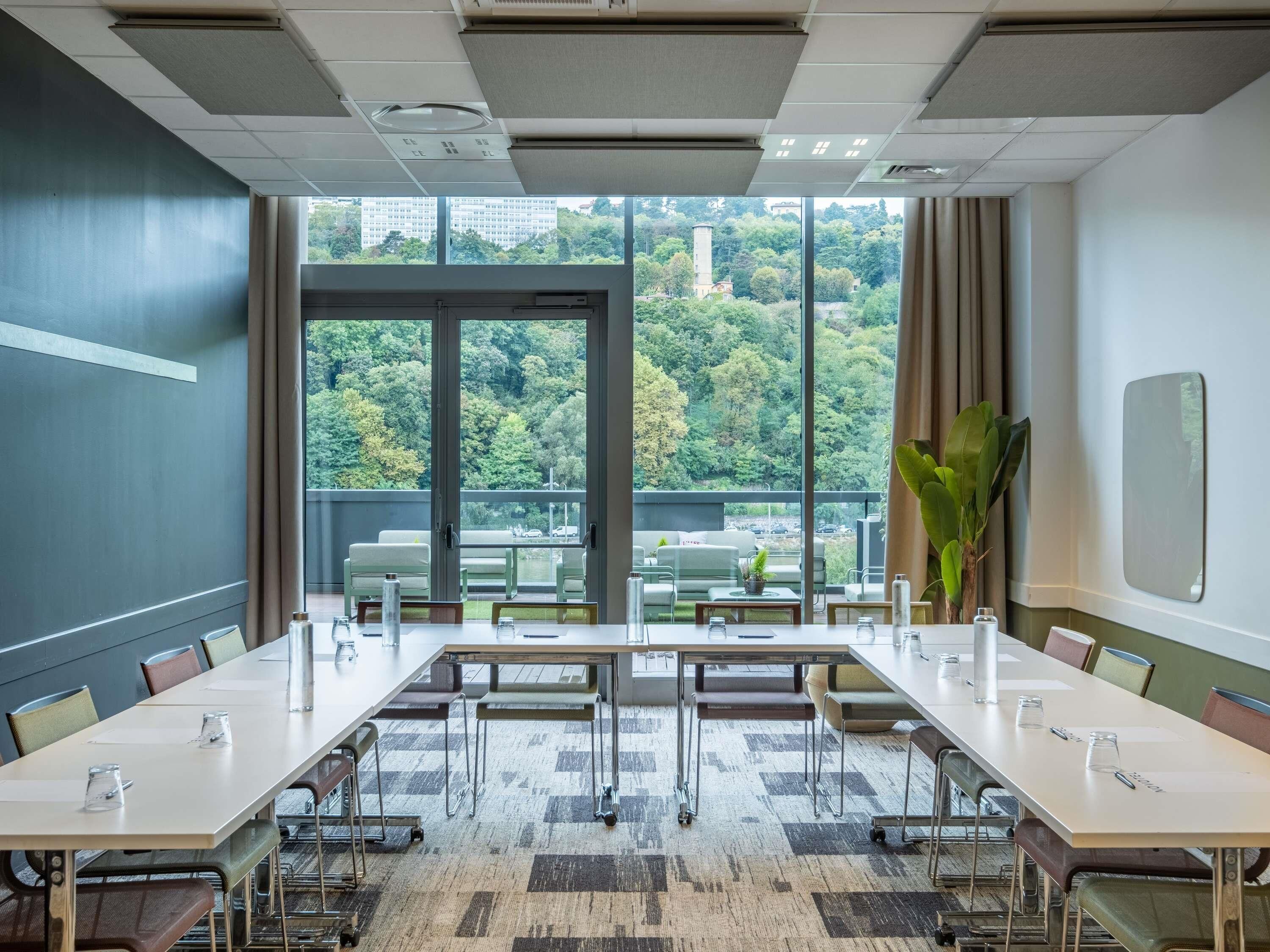 A conference room with a large table, chairs, and a view of a forested area through large windows.