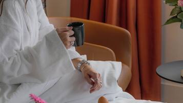 Una persona sentada en una cama con una bandeja de desayuno, que incluye croissants y un vaso de zumo de naranja.