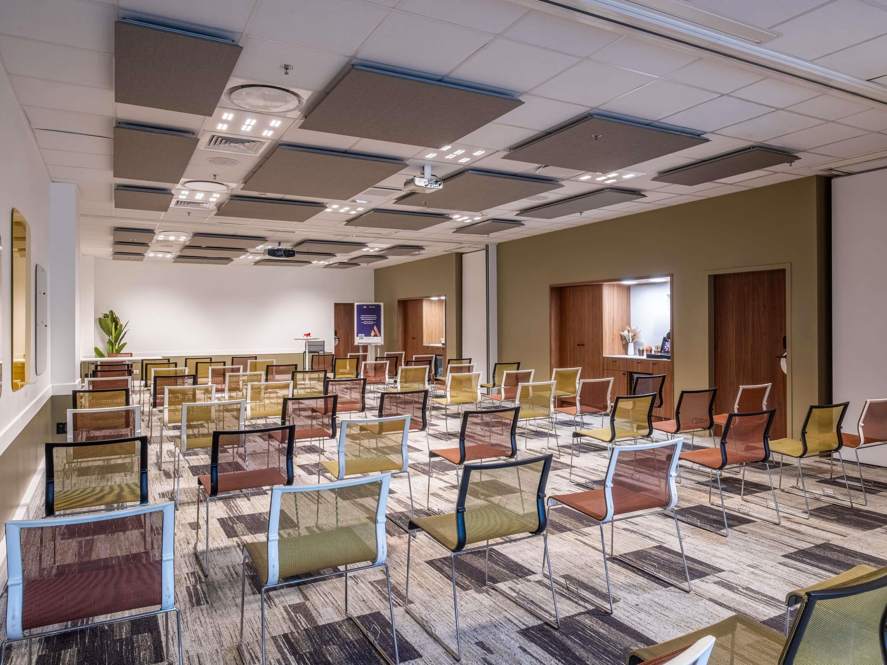 A conference room with rows of chairs, a projector screen, and a carpeted floor.