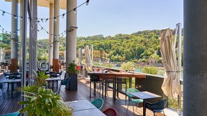 Una terraza con mesas y sillas, vista a un río y un paisaje montañoso al fondo.