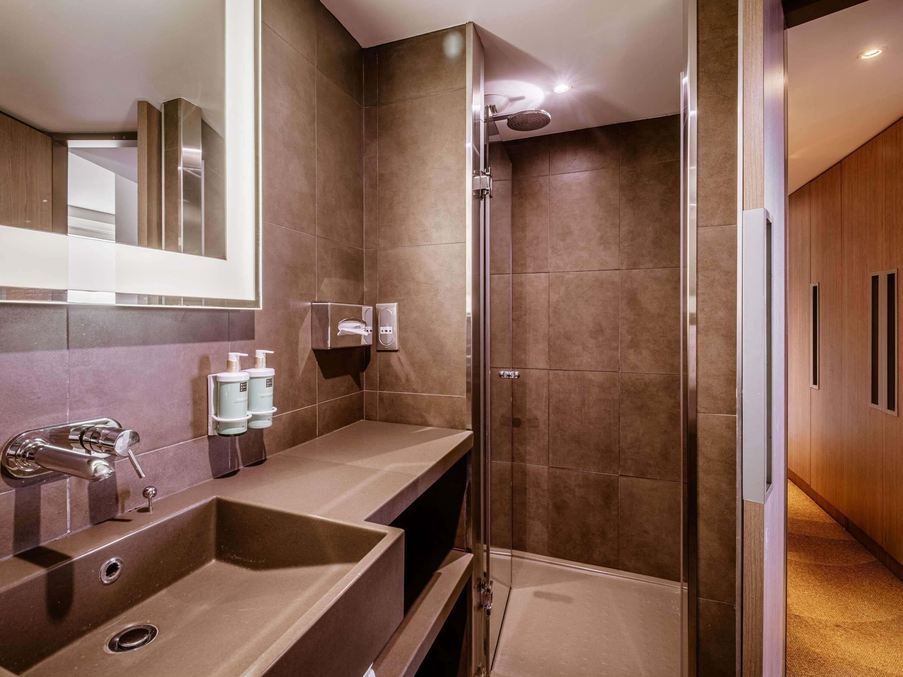 Un baño moderno con un lavamanos grande, espejo y ducha.