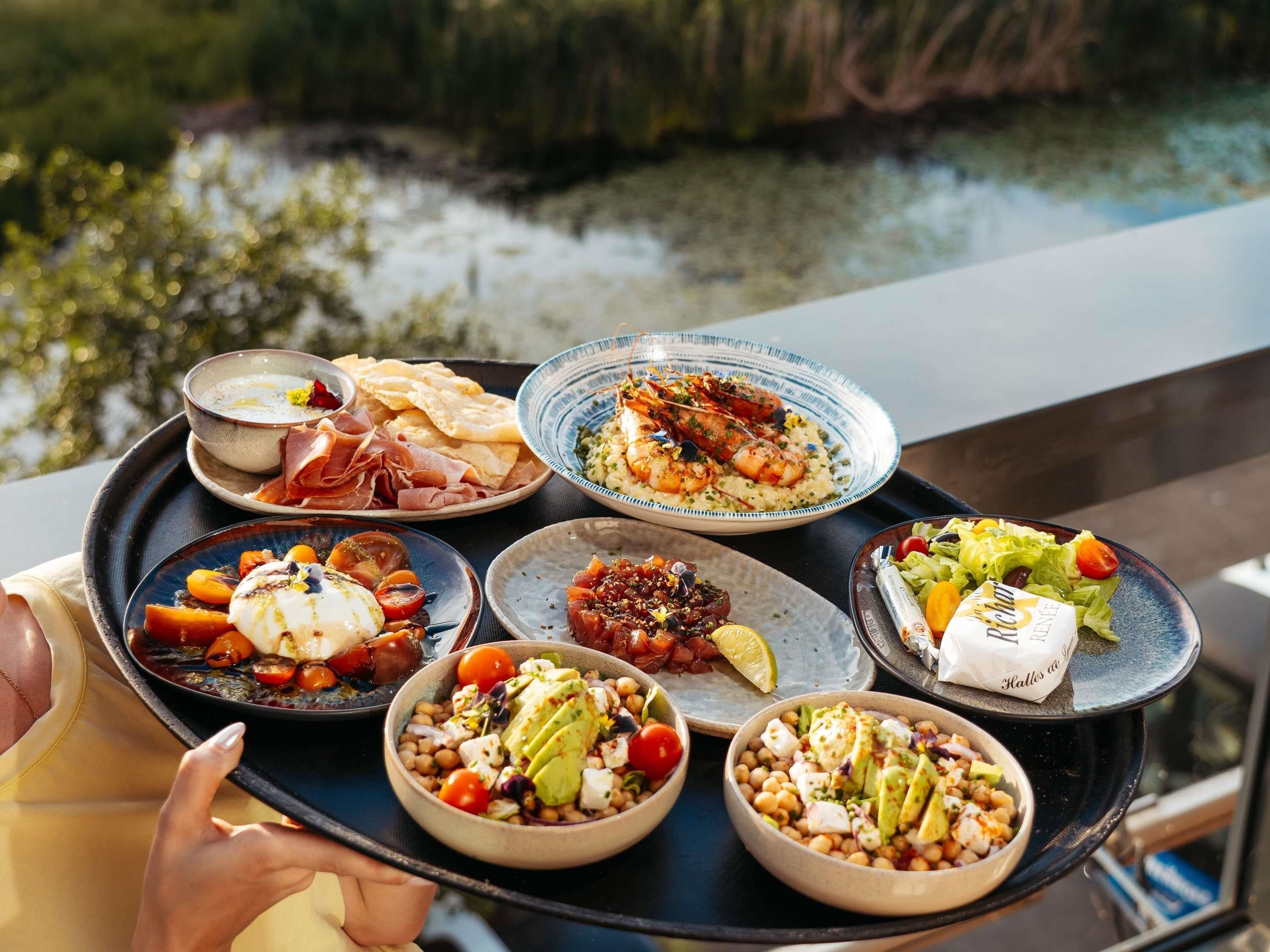 Una bandeja con diversos platos, incluyendo mariscos, ensaladas y carnes, sostenida por una persona.