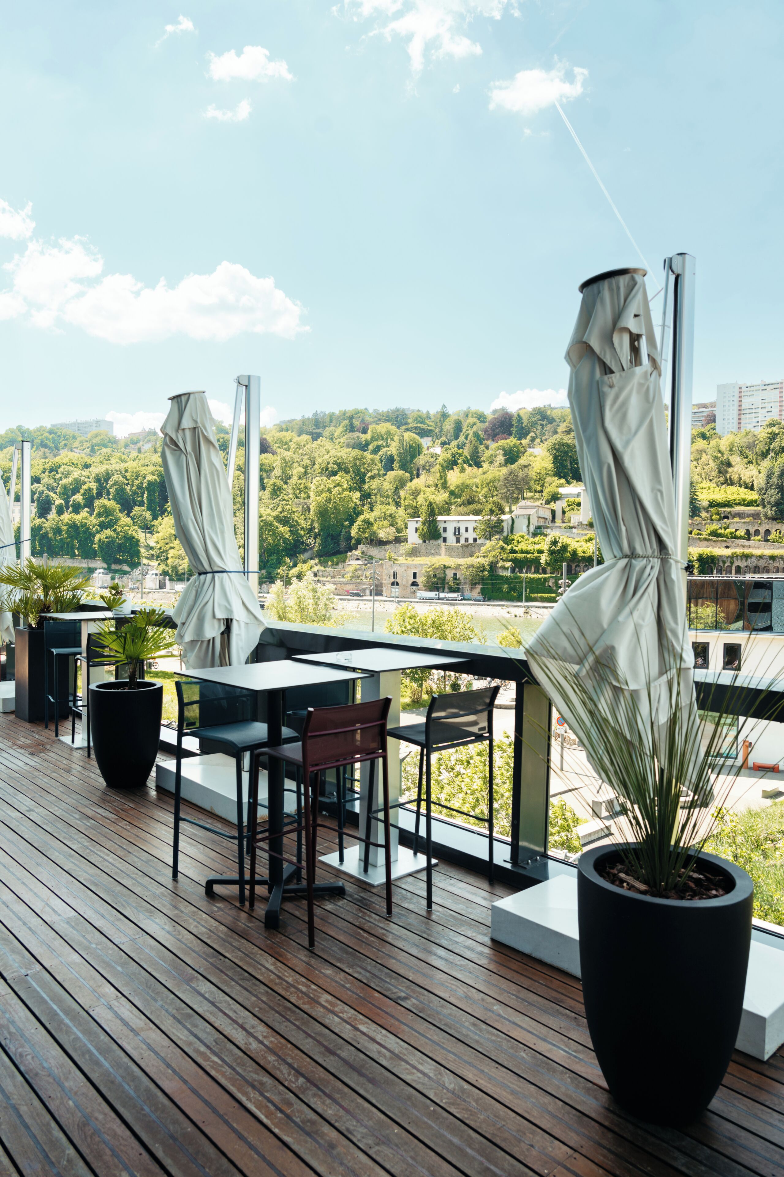 A wooden deck with outdoor seating, potted plants, and a view of a cityscape.