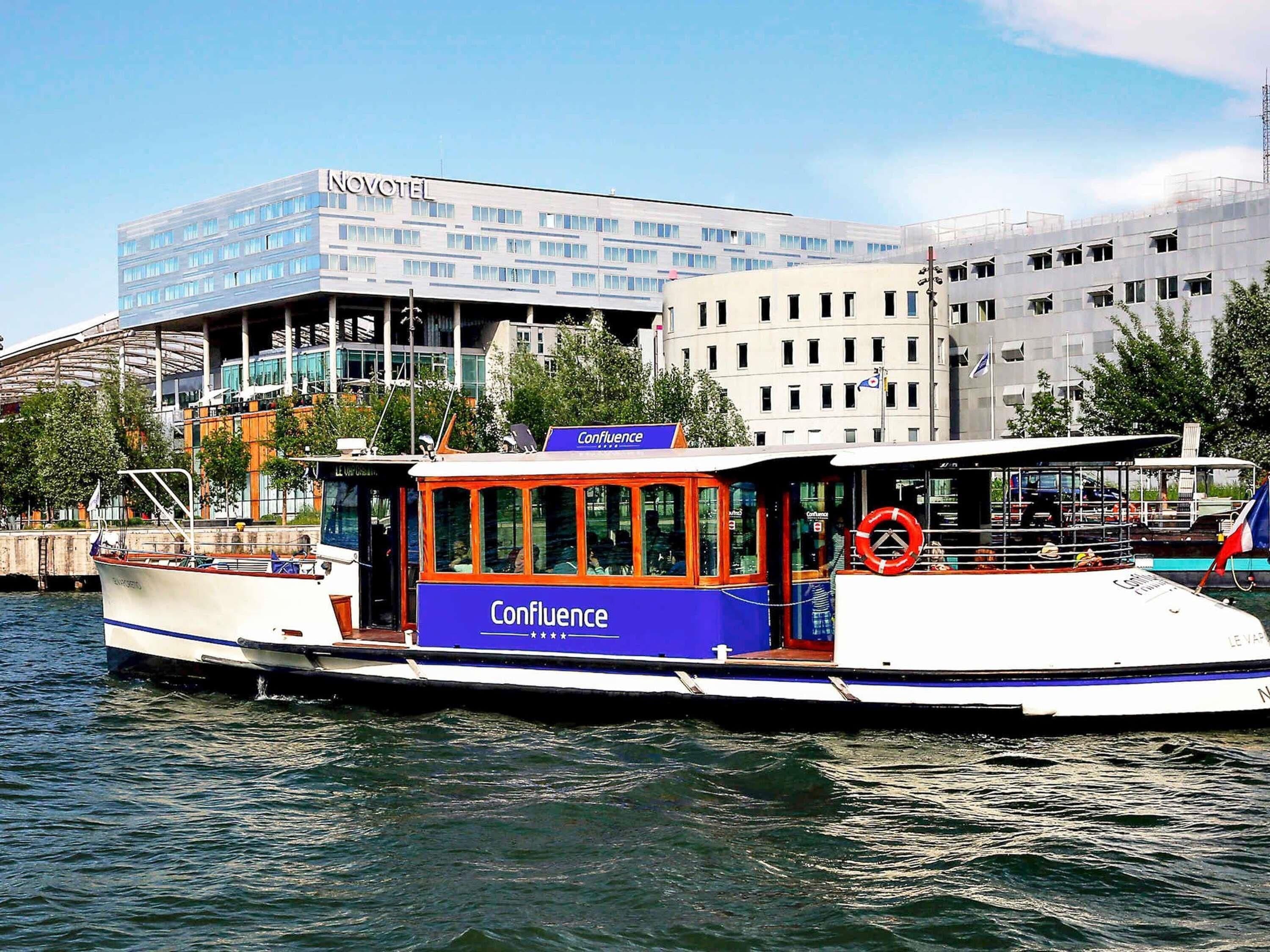 A boat with 'Confluence' written on it, docked near a building labeled 'NOVOTEL.'