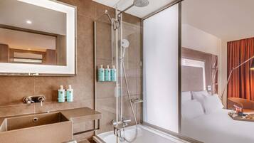 Un baño de hotel moderno con un espejo grande, ducha con cerramiento de vidrio y una bañera.