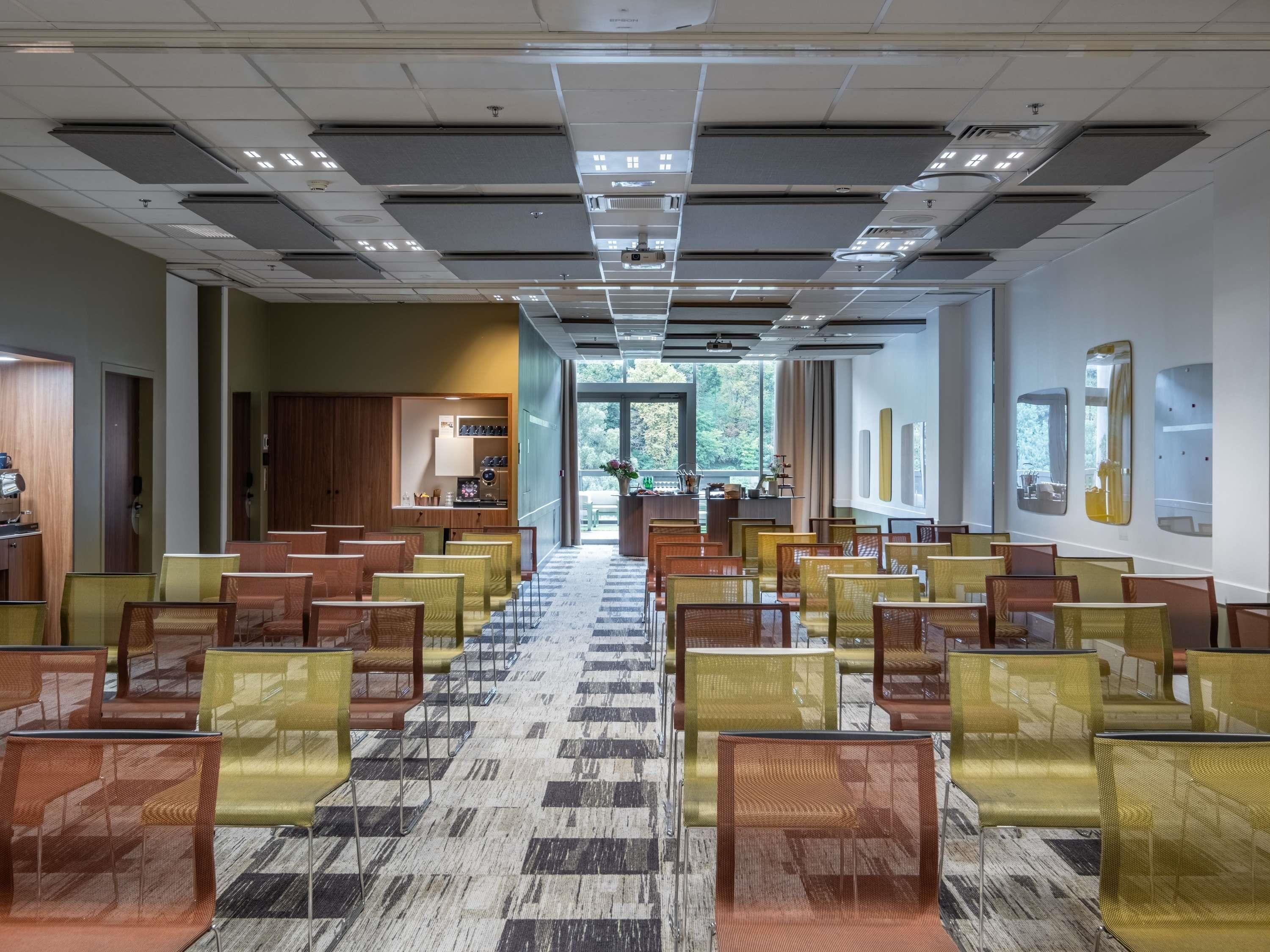 A conference room with rows of chairs, a carpeted floor, and a view through a door to an outdoor area.