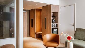 Een moderne kamer met een leren fauteuil, een klein tafeltje met een boek, een bloemenvaas en een kast met een ingebouwde koffiemachine.