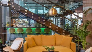 Un interior moderno con un sofá amarillo, dos sillones, una mesa de centro y una escalera con barandilla de vidrio.