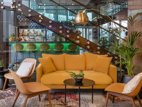 Um interior moderno com um sofá amarelo, duas poltronas, uma mesa de centro e uma escada com guarda-corpo de vidro.
