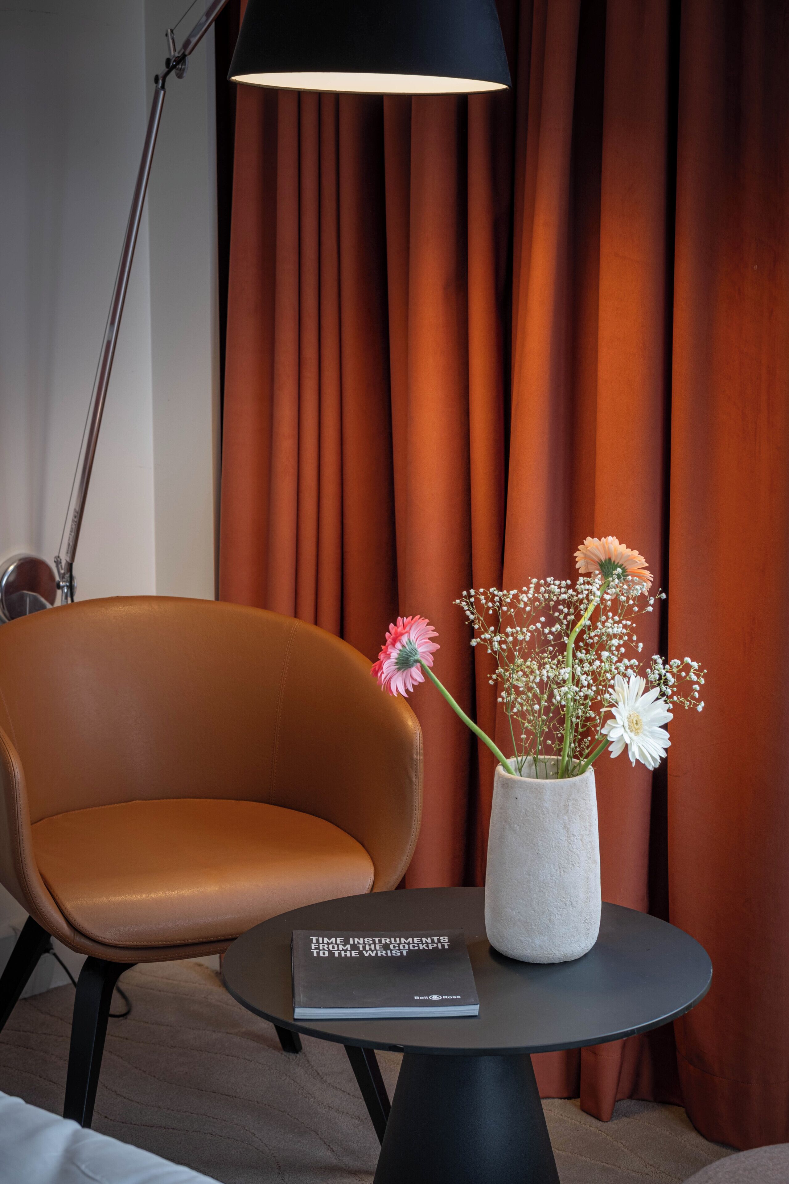 A modern room with a brown leather chair, a round table with a book, and a vase with flowers.