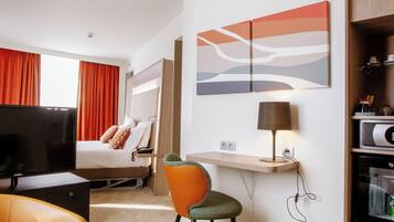 Una habitación de hotel con cama, escritorio, televisión y un área de descanso con sillas.
