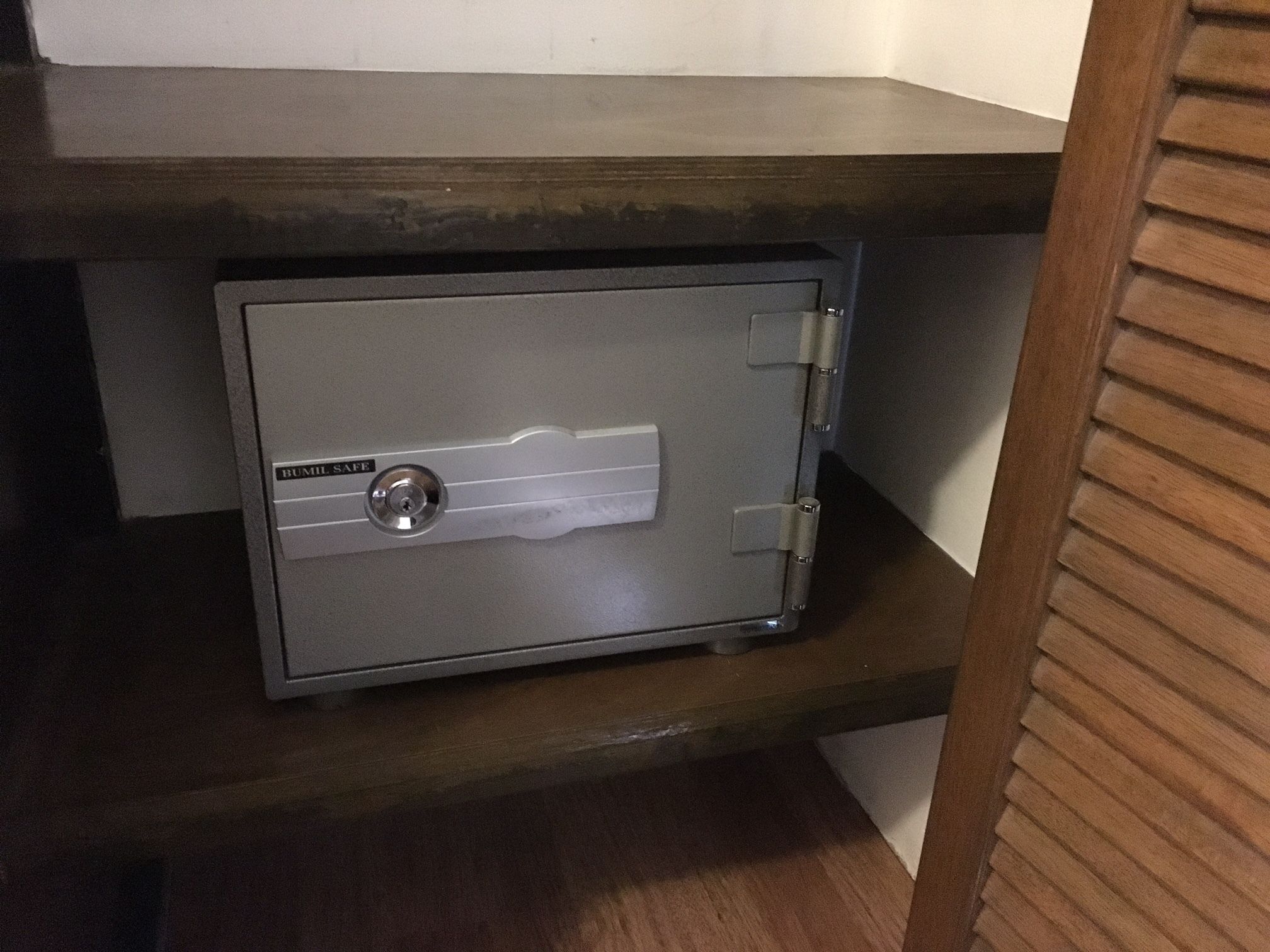 A metal safe with a lock and a label that reads "BULL SAFE" on a wooden shelf.