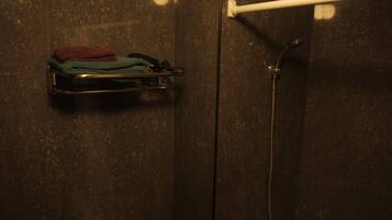 A bathroom with a towel rack holding folded towels, a showerhead, and a hand dryer.