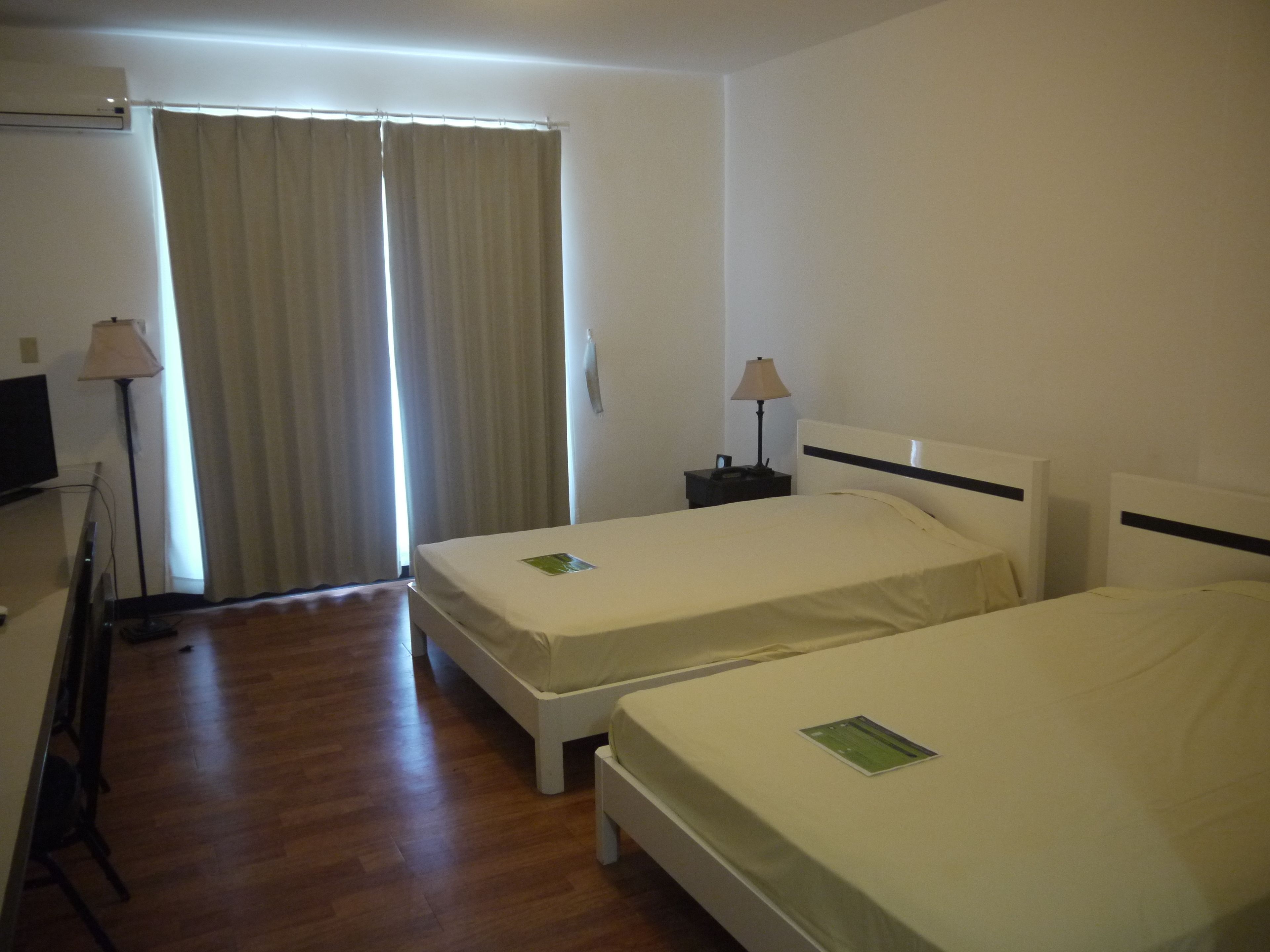 A hotel room with two beds, a desk, a lamp, and a television.