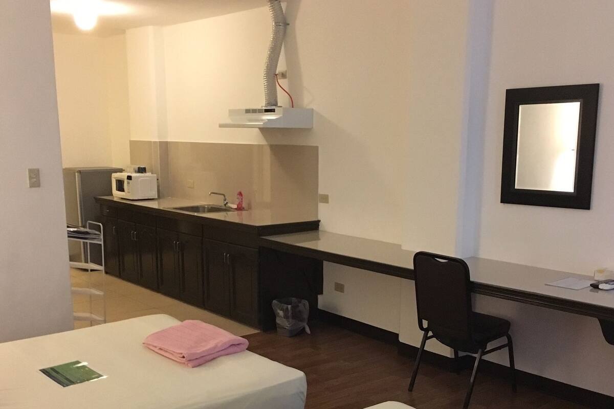 Habitación de hotel con dos camas, un escritorio, una silla, un lavabo y un espejo.
