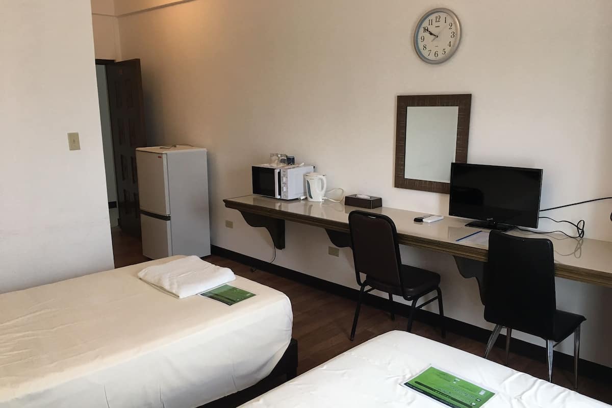 Una habitación de hotel con dos camas individuales, un escritorio con computadora, un microondas y un refrigerador.