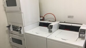 A laundry room with three stacked washing machines and a commercial washer. - Himawari Hotel (Saipan)