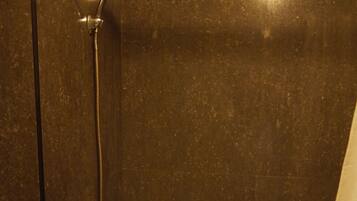 A bathroom with a bathtub, a showerhead, and two bottles of shampoo.