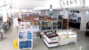 A spacious indoor market with various stalls selling goods, including a refrigerated display case and shelves stocked with bottled water.