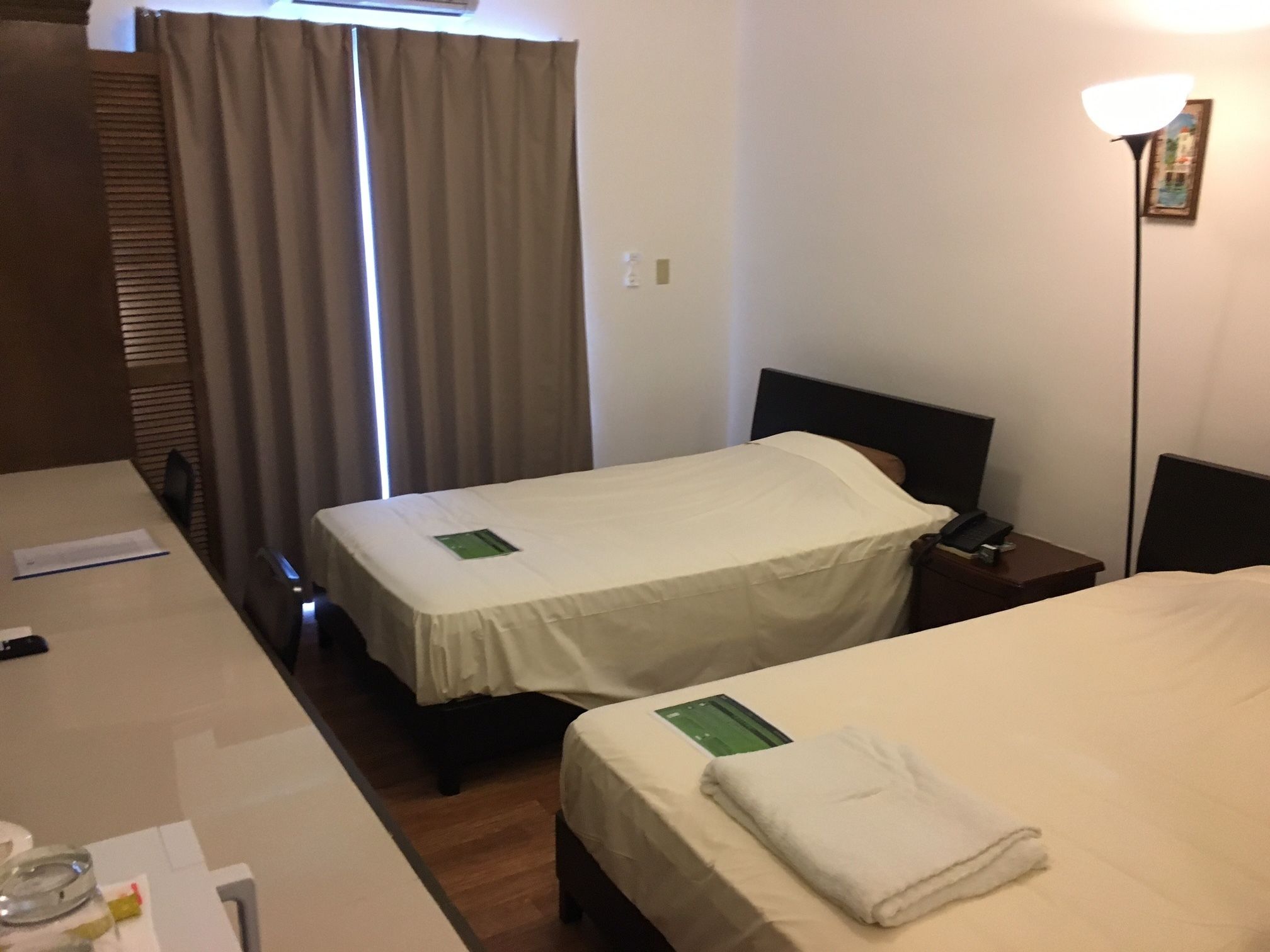 A hotel room with two beds, a desk with a chair, a lamp, and a window with curtains.
