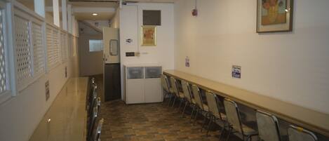 A hallway with a long table and chairs, a refrigerator, and a door leading to another room.