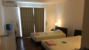 A hotel room with two beds, a desk with a computer, a lamp, and a window with curtains. - Himawari Hotel (Saipan)