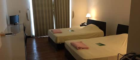 Habitación de hotel con dos camas, un escritorio con computadora, una lámpara y una ventana con cortinas.
