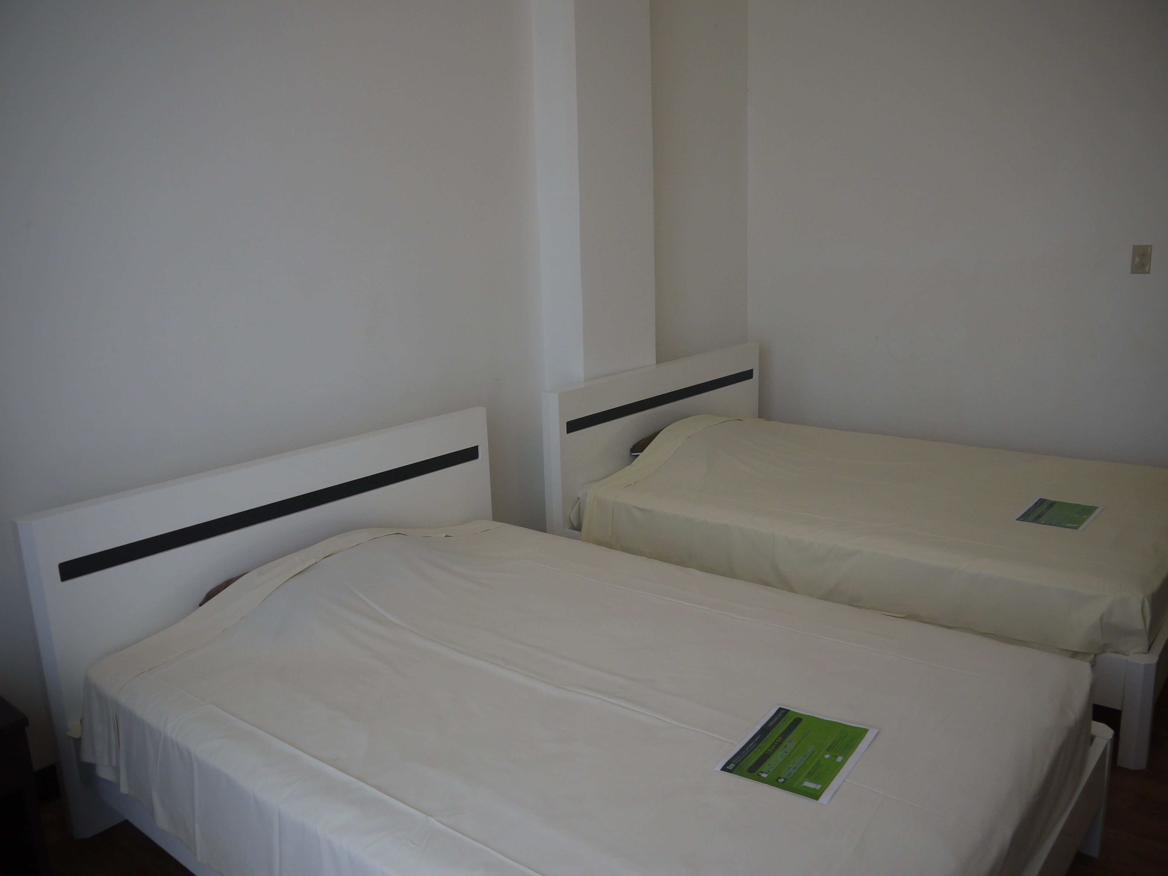 Two single beds with white linens and black headboards in a room with plain white walls.
