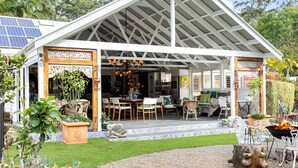 Un área de comedor al aire libre cubierta con techo blanco, una mesa con sillas y plantas en macetas.
