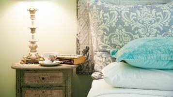 Een keurig opgemaakt bed met een gestreept kussen en een blauw sierkussen, een nachtkastje met een lamp, een boek en een theekopje.