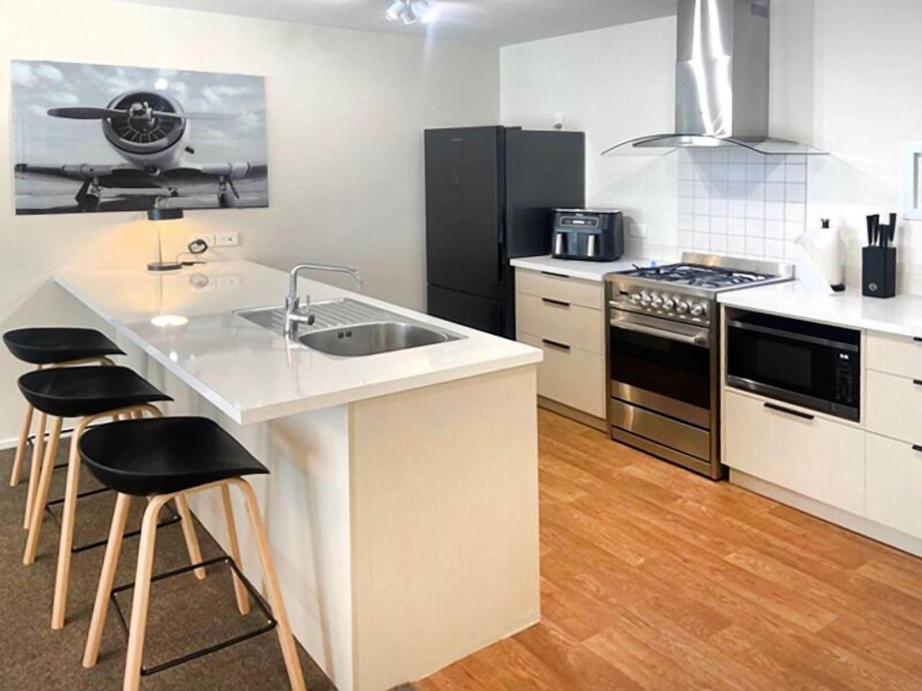 A modern kitchen with a central island, stainless steel appliances, and black bar stools.
