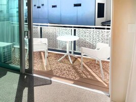 Un balcón con sillas blancas, una pequeña mesa, un ventanal de vidrio y una pared con diseño.