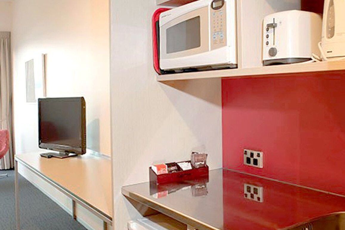 A hotel room with a flat-screen TV, a microwave, a toaster, and a red minibar.