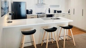A modern kitchen with a central island, bar stools, a refrigerator, a stove, and a sink.