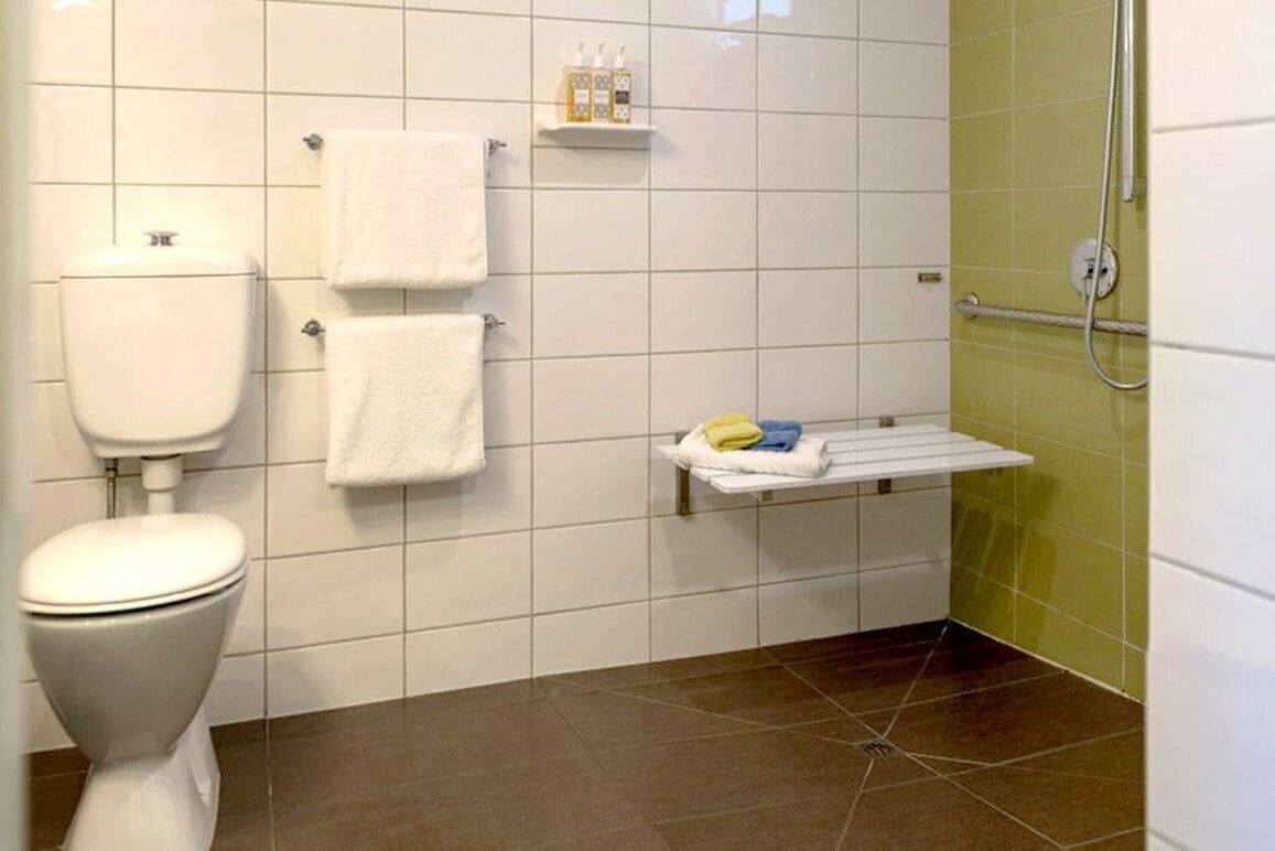 Une salle de bain comprenant des toilettes, deux serviettes blanches, une étagère avec des articles de toilette et un espace douche.