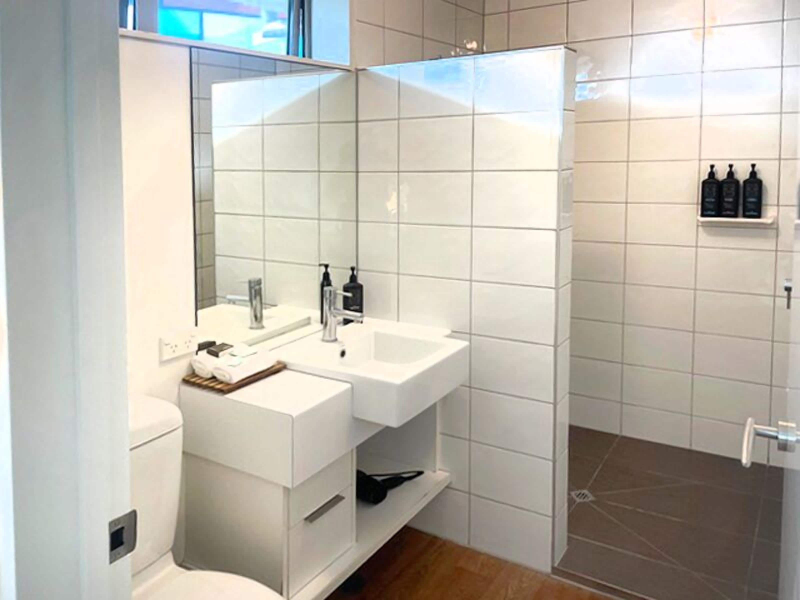 Een moderne badkamer met een wit wastafelmeubel, een grote spiegel en een douchehoek.