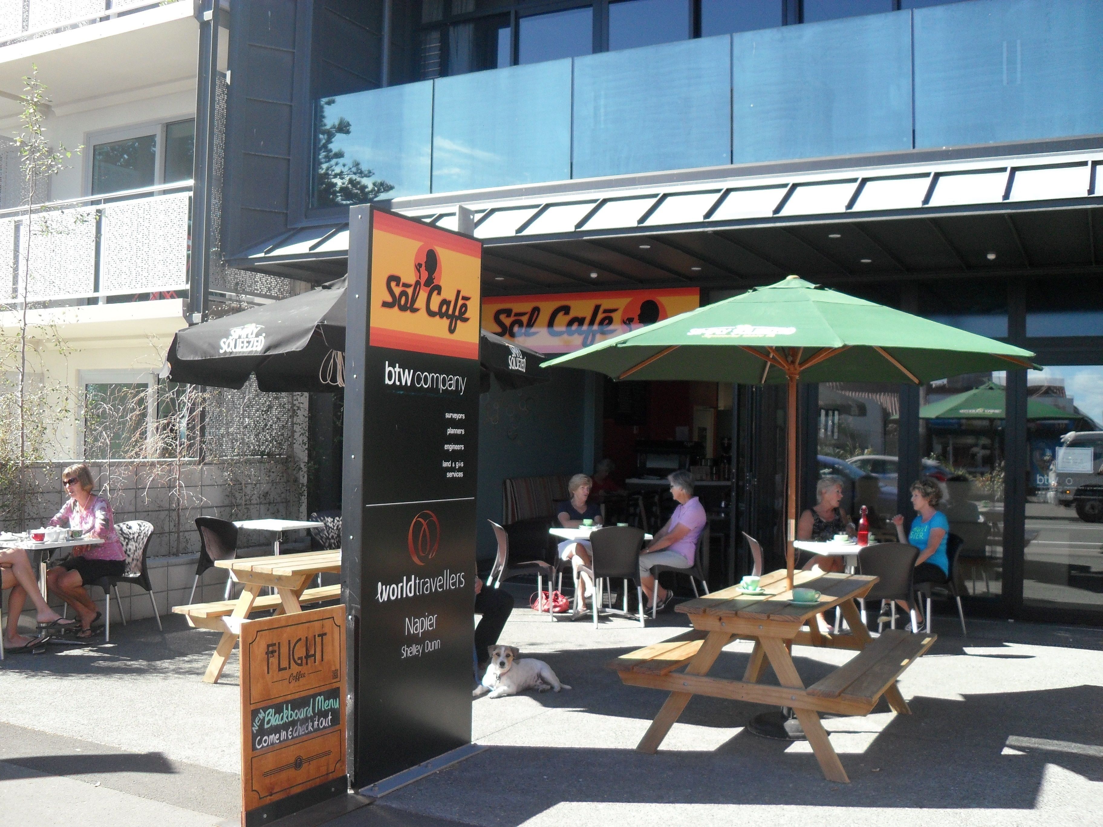 An outdoor seating area with tables and chairs, a sign for 'Sol Café', and a blackboard menu board.