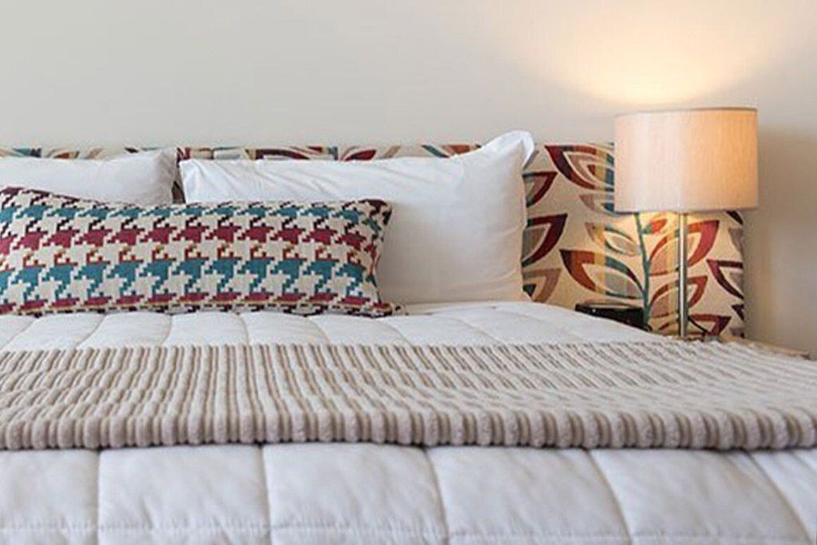 Un lit bien fait, agrémenté d’un coussin à motifs et d’une lampe au design géométrique.
