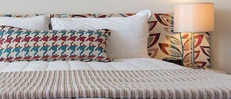 Un lit bien fait, agrémenté d’un coussin à motifs et d’une lampe au design géométrique.