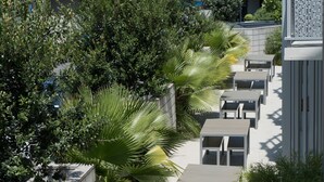 A pathway lined with outdoor seating, surrounded by lush greenery and a modern building with a balcony.