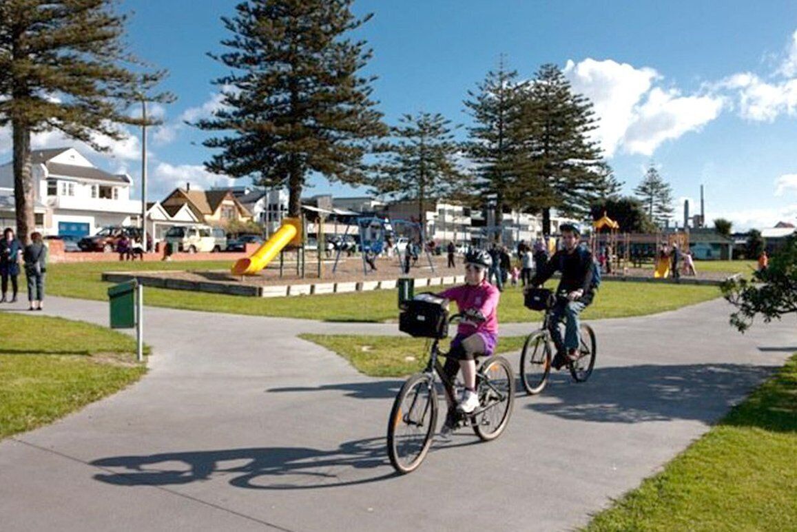 A paved pathway in a park with cyclists and a playground.