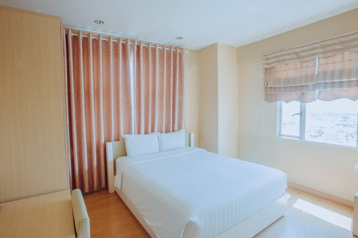 A bedroom with a bed, curtains, a window with a view, and a wardrobe.